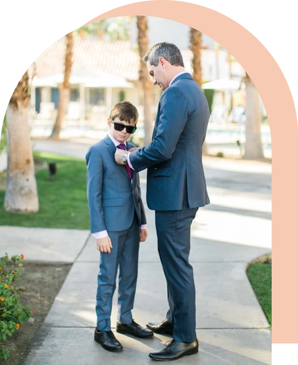 A man and boy in suits standing on the sidewalk.